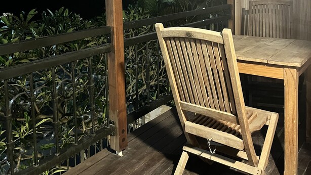 A wooden deck with a table and chairs, surrounded by a metal railing and plants. - Flic En Flac: Furnished 2 bedrooms  1 min walk from beach with WIFI & Nespresso (Flic- en-Flac)