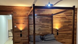 A four-poster bed with a wooden frame and grey bedding, positioned against a wall with wooden paneling and two wall-mounted lights. - Flic En Flac: Furnished 2 bedrooms  1 min walk from beach with WIFI & Nespresso (Flic- en-Flac)
