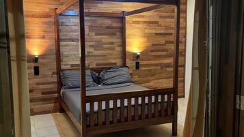 Ein Himmelbett mit Holzrahmen und grauer Bettwäsche, vor einer Wand mit Holzvertäfelung und zwei Wandleuchten.