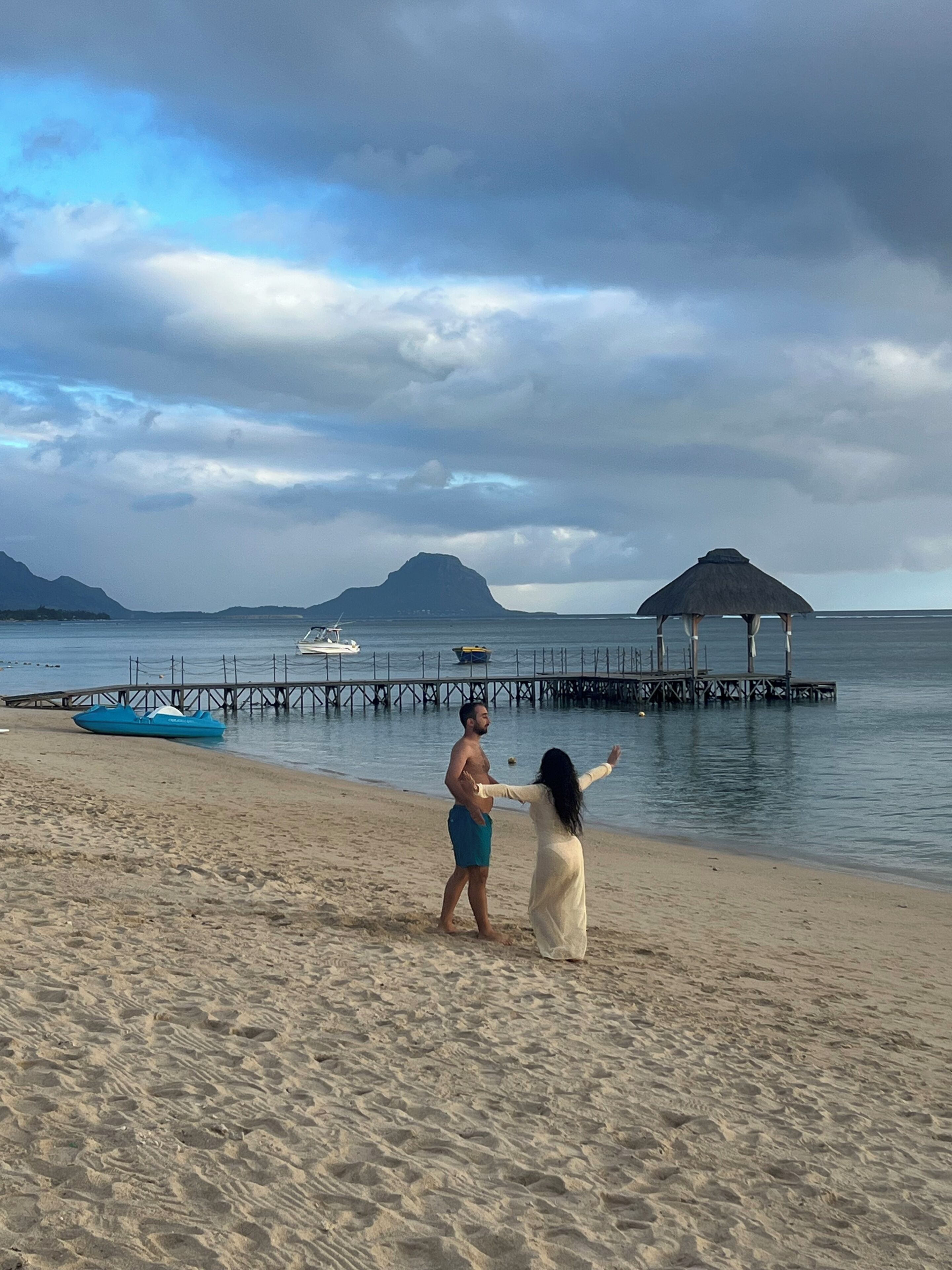 A beach with a pier, a boat, and a thatched-roof structure.