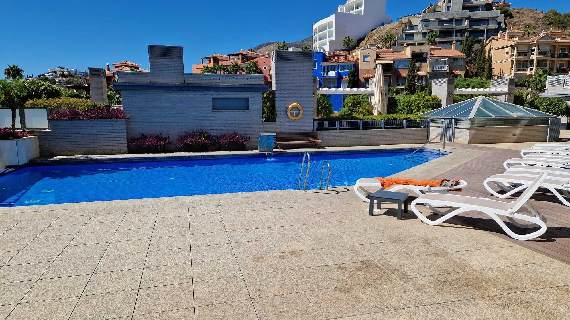 A swimming pool with a clear blue water, surrounded by lounge chairs and a tiled deck.