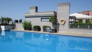 Une piscine avec un bâtiment moderne en arrière-plan, une bouée de sauvetage et des plantes en pot.