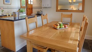 A wooden dining table with a fruit platter, a kitchen island with a toaster, and a white water heater.