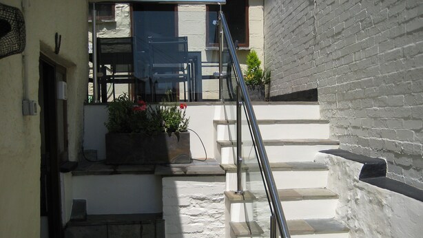 A narrow stairway with a metal handrail, leading to a landing with a potted plant and a door.