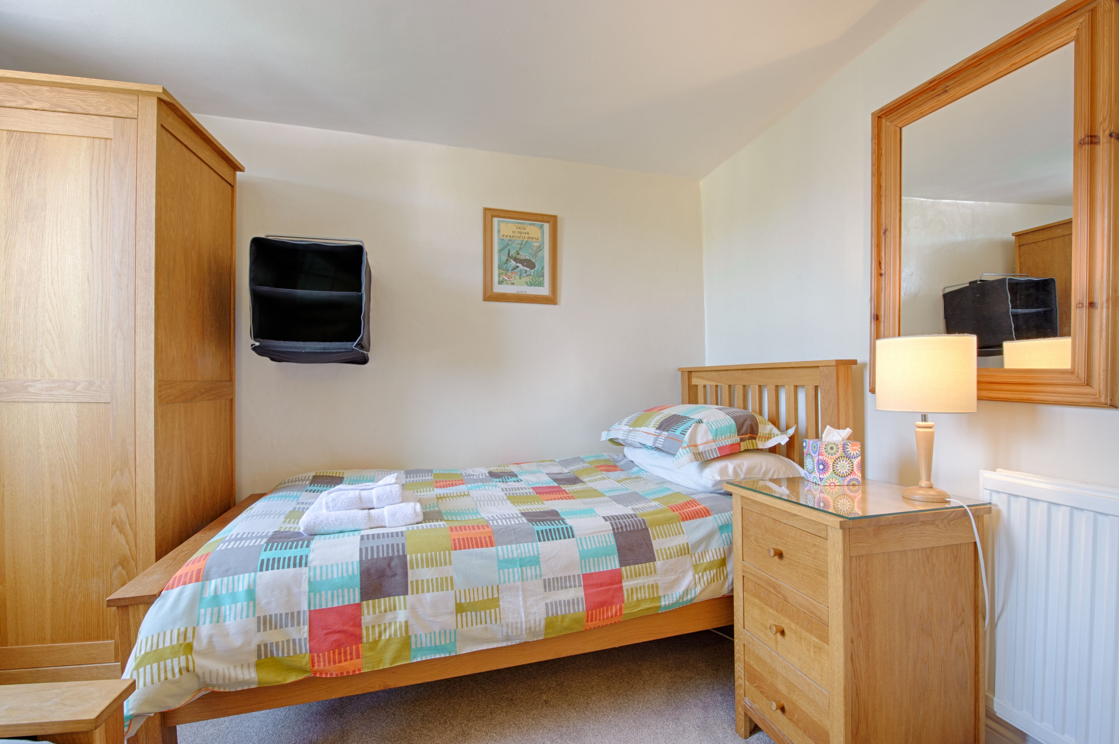 Ein Schlafzimmer mit einem hölzernen Bett, einem Schminktisch, einem Spiegel und einem an der Wand befestigten Fernseher.