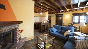 Una sala de estar con chimenea, un sofá, una mesa de centro y una cocina al fondo.