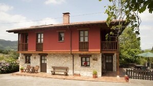 Una casa de dos pisos con fachada de piedra, balcón de madera y un pequeño porche con un banco.
