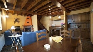 Una sala de estar acogedora con chimenea, vigas de madera en el techo, una mesa de comedor con sillas y una zona de cocina con armarios de madera.