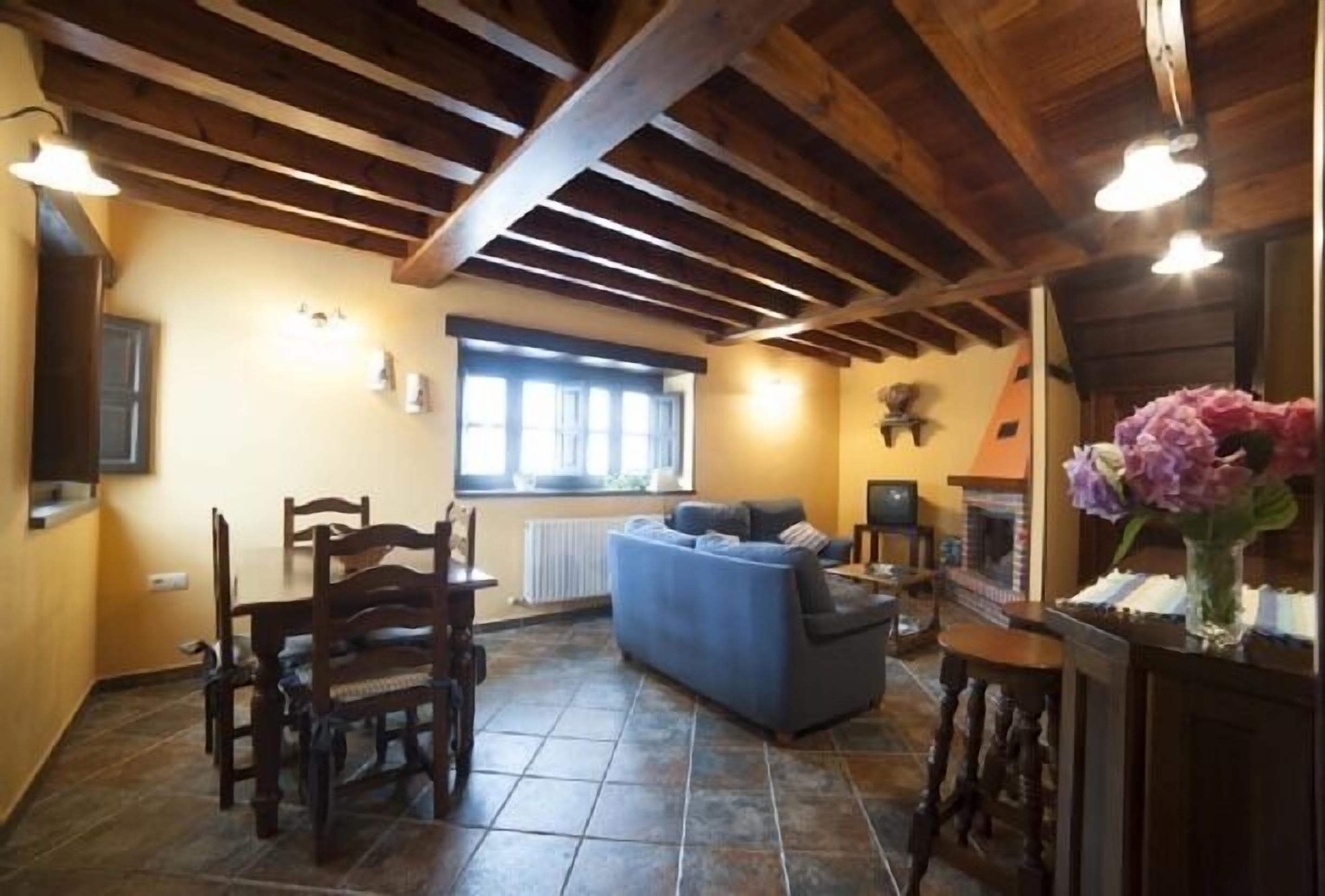 Una sala de estar acogedora con un sofá, sillas de madera, una chimenea y un comedor con mesa y sillas.