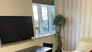 Un soggiorno con una TV a schermo piatto montata a parete, un tavolo da pranzo con sedie, una pianta in vaso, un divano e un tappeto decorato.