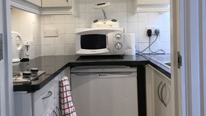 Una cucina compatta con mobili bianchi, un forno a microonde, una lavastoviglie e un piccolo ripiano con oggetti decorativi.