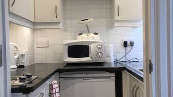 A compact kitchen with white cabinets, a microwave, a dishwasher, and a small shelf with decorative items.