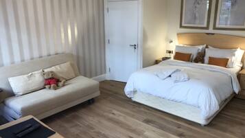 A hotel room with a bed, a sofa, a small table with a remote control, and a wardrobe.