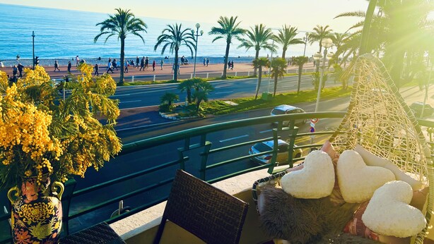 Een balkon met uitzicht op het strand, palmbomen en een sierplant.