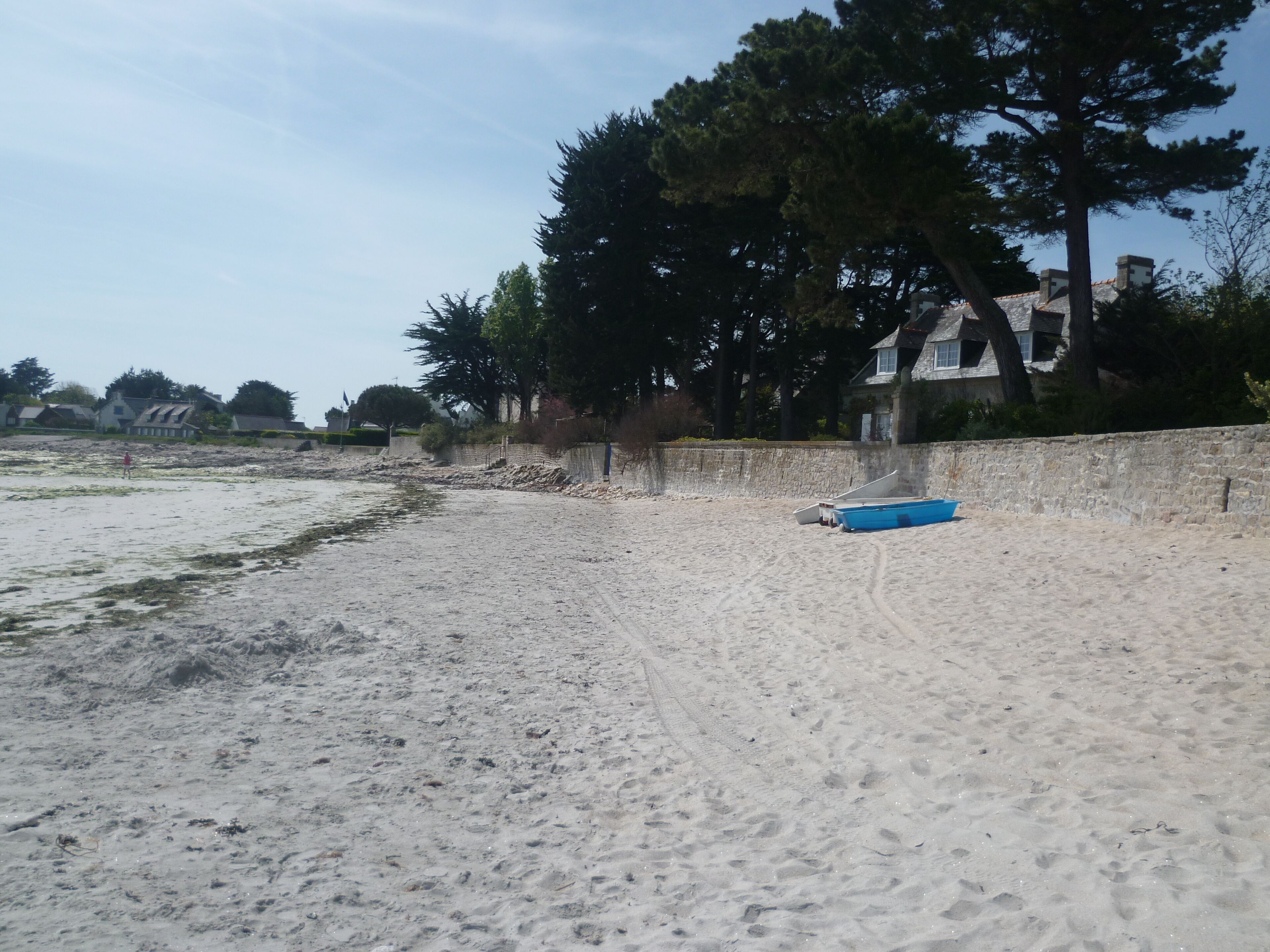 A sandy beach with a blue boat and a stone wall.