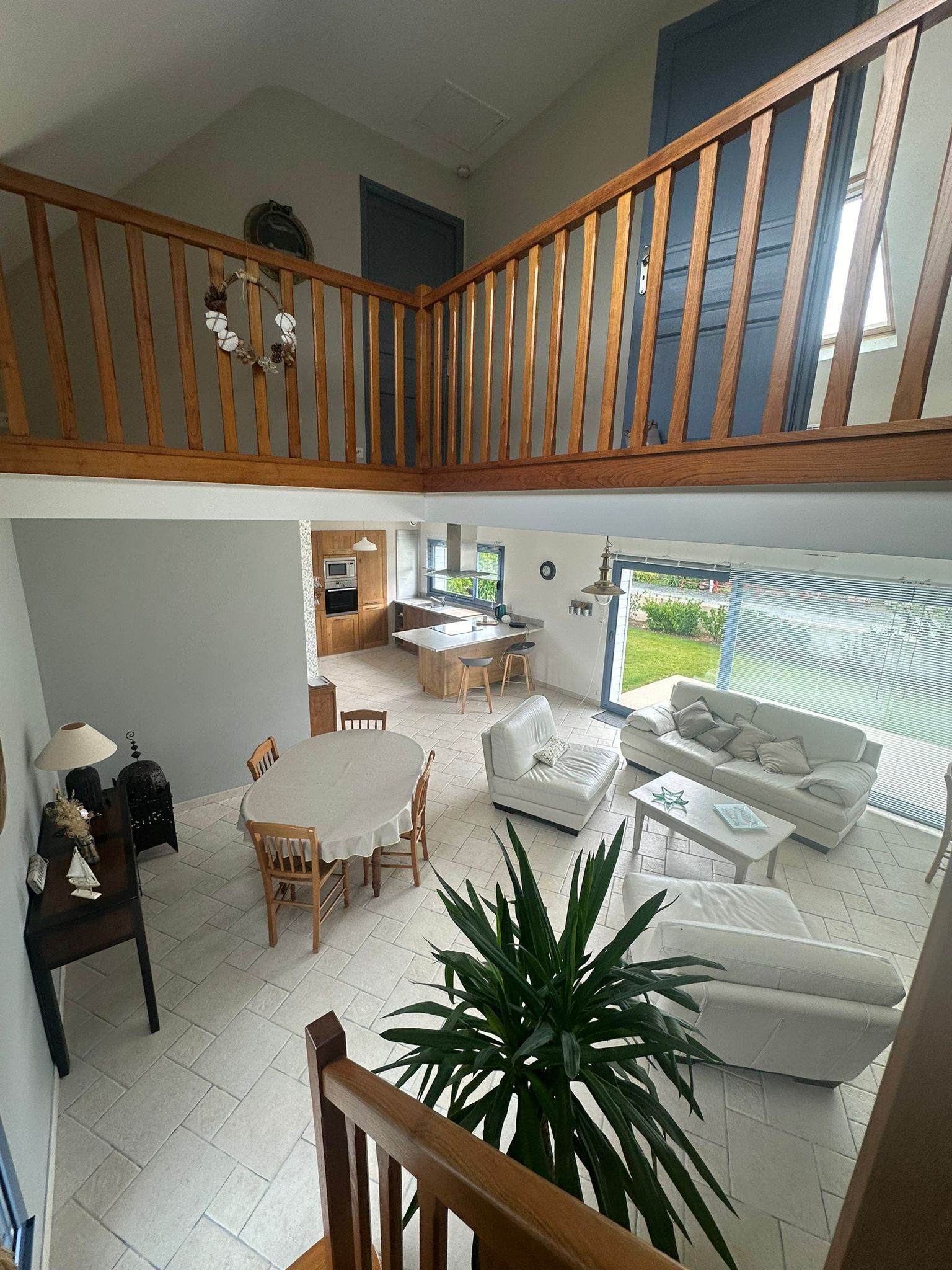 Un'ampia zona giorno con soffitto alto, ringhiera in legno, un tavolo da pranzo con sedie, un divano e una cucina sullo sfondo.