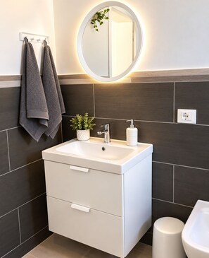 A modern bathroom with a white sink, a mirror, a towel rack, a potted plant, and a bidet.