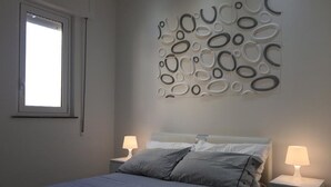 A bedroom with a bed, two bedside tables with lamps, a window, and a wall with circular patterns. - Casa Anna 800 meters from the SEA .... (Balestrate)