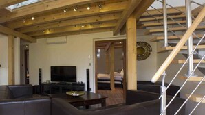 Uma sala de estar moderna com teto de madeira, televisão, sofás de couro e escada.