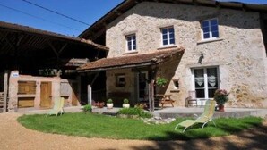 A stone building with a sloped roof, a porch with chairs, and a small garden area. - Saint Romans: Country holiday home - St romans (Saint-Romans)