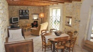 A rustic room with stone walls, a wooden ceiling, a bed, a sofa, a dining table with chairs, a TV, and a lamp. - Saint Romans: Country holiday home - St romans (Saint-Romans)