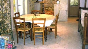 A dining area with a round table and wooden chairs, a stone wall, and a door leading outside. - Saint Romans: Country holiday home - St romans (Saint-Romans)
