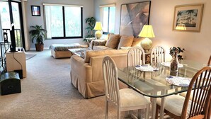 A living room with a glass dining table, beige sofas, and a large window. - Bright, corner unit, with open floor plan and views from nearly every room!  (Bradenton Beach, Anna Maria Island)