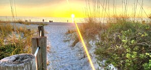 A beach path leading to the sea with a wooden post and vegetation on the sides.