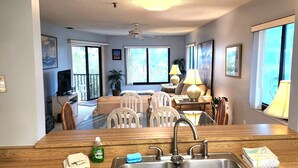A kitchen with a sink, a dining table with chairs, a ceiling fan, and large windows. - Bright, corner unit, with open floor plan and views from nearly every room!  (Bradenton Beach, Anna Maria Island)