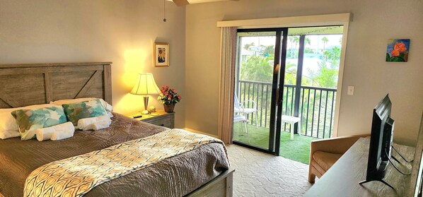 A bedroom with a bed, a nightstand with a lamp, a TV, and a balcony with outdoor furniture.