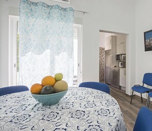 Un comedor con una mesa lista para cuatro, un frutero y una cocina a la vista.