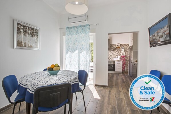 A dining area with a table set for two, a bowl of fruit, and a framed picture on the wall.