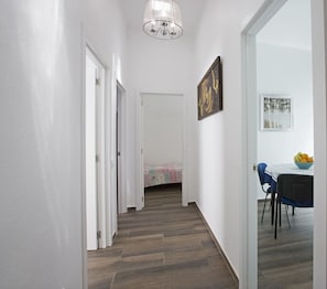 Um corredor com piso de madeira, paredes brancas e uma sala de jantar com mesa e cadeiras.
