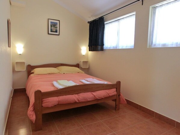 A bedroom with a wooden bed, two bedside lamps, a window with curtains, and a wall-mounted picture.