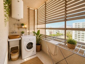 A compact laundry area with a washing machine, drying rack, and potted plants.
