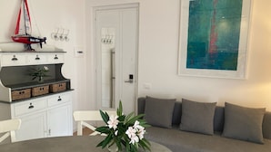 A modern living room with a grey sofa, a round table with a vase of flowers, a white cabinet with wicker baskets, and a sailboat model on the cabinet. - Apartment with direct access to lake and close to dog park  (Sirmione)