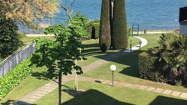 A landscaped garden with a view of the sea, featuring neatly trimmed hedges and a pathway. - Apartment with direct access to lake and close to dog park  (Sirmione)
