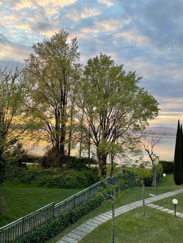 A garden with a pathway, trees, and a view of a body of water. - Apartment with direct access to lake and close to dog park (Sirmione)