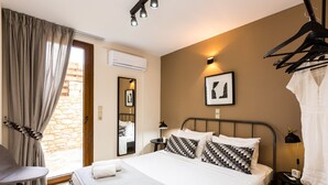 A hotel room with a bed, a chair, a small table, a hanging light, and a wall-mounted air conditioner. - Aestas Residence, Refined Summer Retreat with Pool, Spa Whirlpool & Ping Pong (Rethymno)