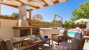 An outdoor patio with a brick fireplace, wooden furniture, and a pool area. - Aestas Residence, Refined Summer Retreat with Pool, Spa Whirlpool & Ping Pong (Rethymno)