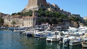 A marina with boats docked, a historic fort on a hill, and buildings along the waterfront. - Large charming duplex, air-conditioned and WiFi in the heart of the citadel  (Bonifacio)