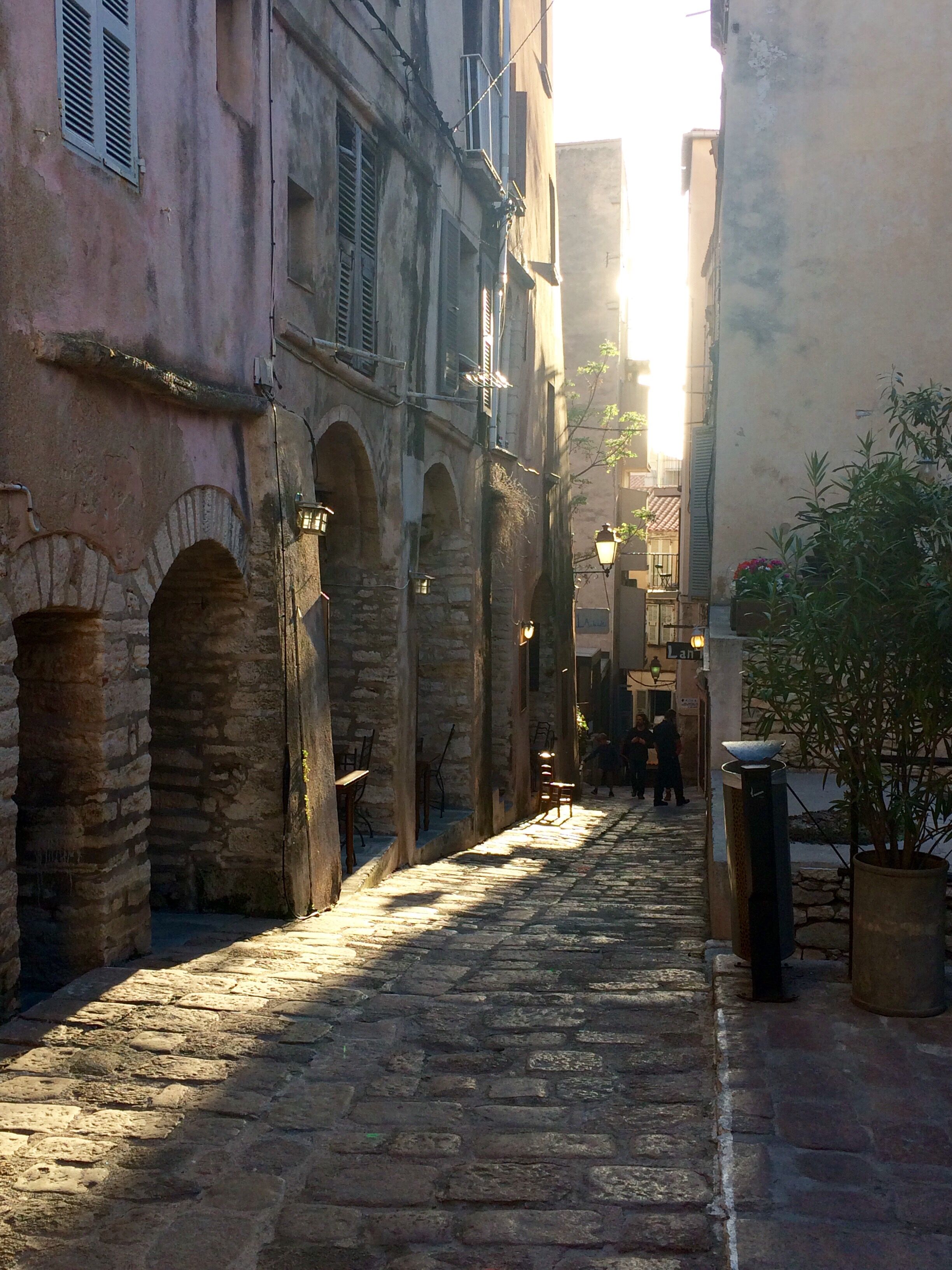 A narrow cobblestone street flanked by historic buildings with stone arches and traditional architecture.