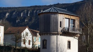 A white building with a red door, a balcony, and a mountain backdrop.