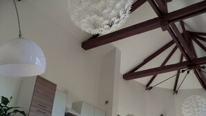 A kitchen with wooden beams, white cabinets, and a hanging white chandelier.