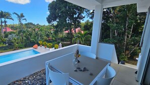 A balcony with a pool, outdoor seating, and a view of a lush garden and buildings. - Chic Room in a beautiful 1930s Art Deco property (Petit Bourg)