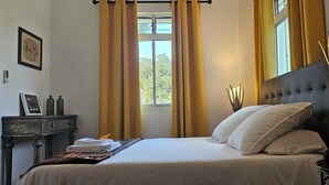 A neatly made bed with white linens, a bedside table with a lamp, and a window with curtains. - Chic Room in a beautiful 1930s Art Deco property (Petit Bourg)