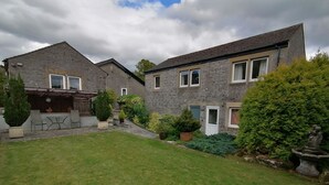 A two-story stone house with a well-maintained lawn, potted plants, and a small garden area. - Comfortable and spacious apartment in Middleton-by- Youlgrave near Bakewell.  (Middleton-by-Youlgrave)