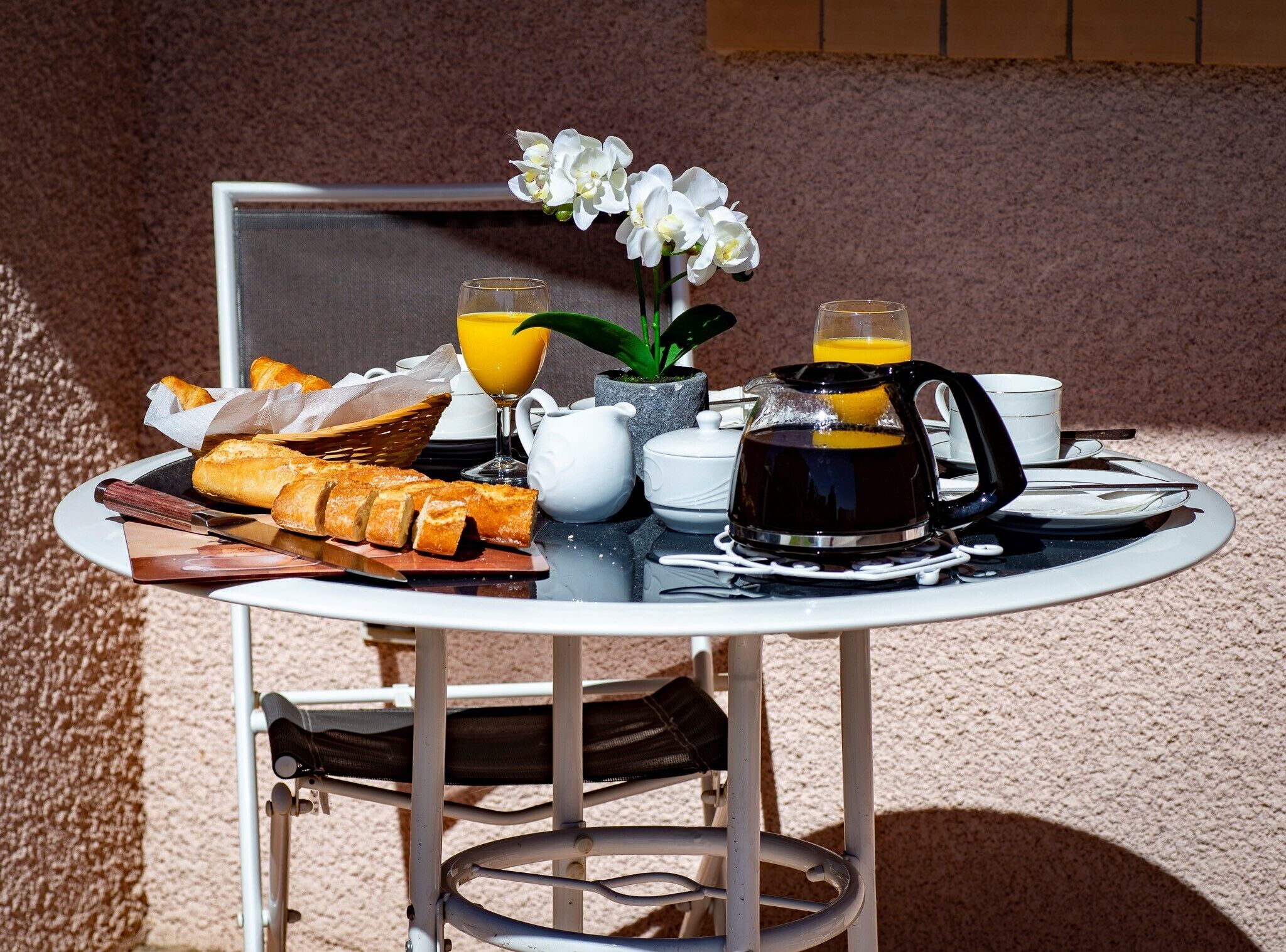 Uma mesa externa com café da manhã, incluindo croissants, suco de laranja, café e uma flor.