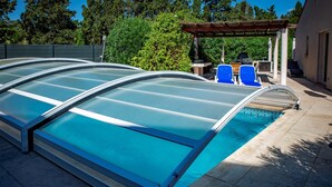 Uima-allas, jossa on lasiseinäinen allasalue, siniset tuolit ja pergola.