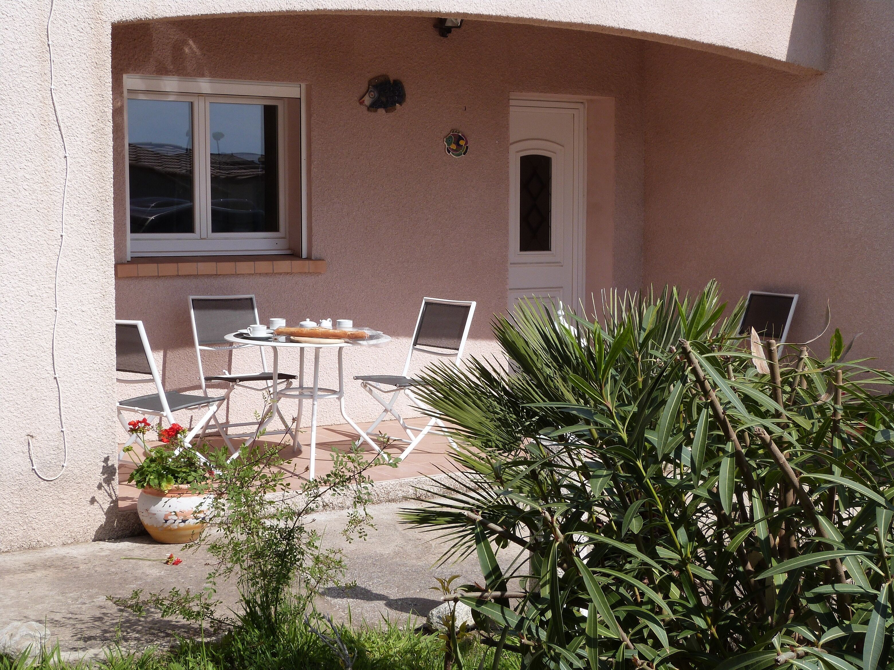 An outdoor patio with a round table and four chairs, a potted plant, and a door.